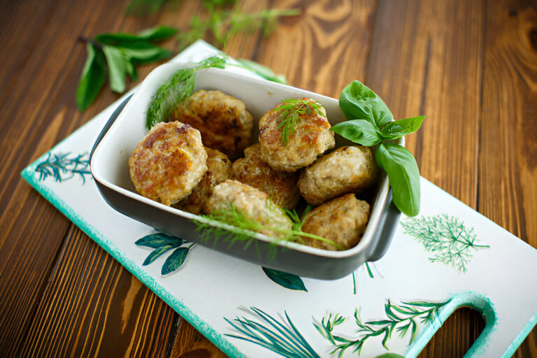A serving of golden-brown meatballs garnished with fresh herbs in a rectangular dish on a decorative platter.