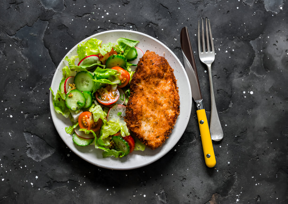A plate of crispy fried chicken served with a fresh salad on a dark textured surface.