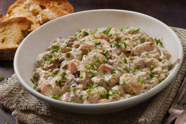 A creamy shrimp dish garnished with parsley served in a white bowl alongside toasted bread.