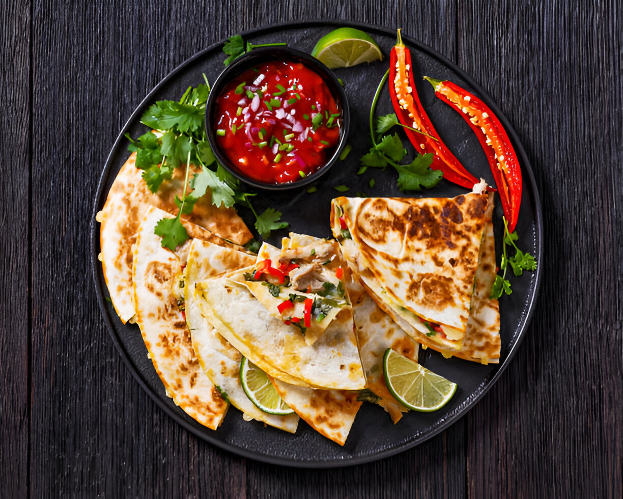 A plate of assorted quesadillas served with salsa, fresh cilantro, lime, and red chili peppers.