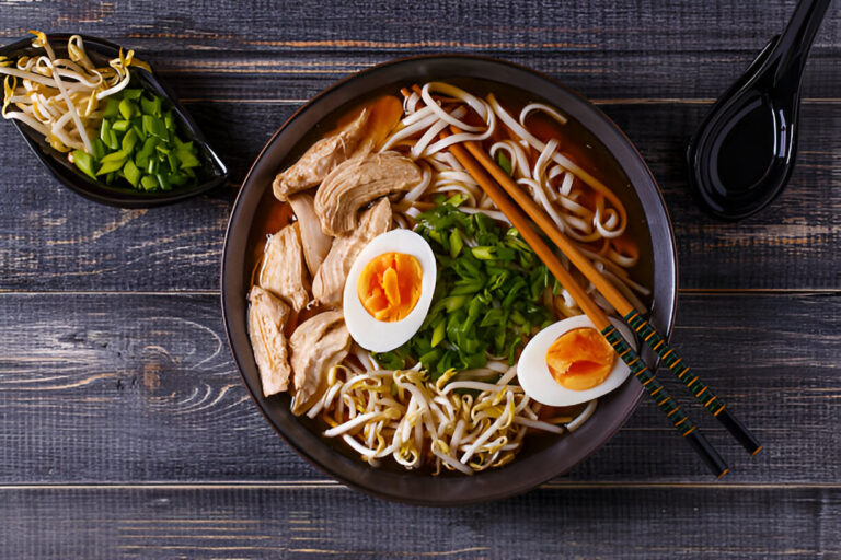 A bowl of delicious ramen with chicken, boiled eggs, green onions, and bean sprouts, accompanied by a side of chopped green vegetables.