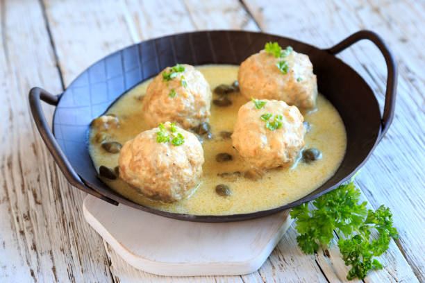 A cast iron pan containing four meatballs in a creamy sauce, garnished with green herbs.
