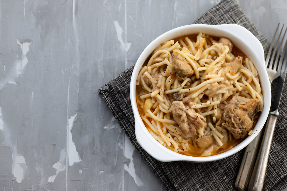 A bowl of spaghetti with chicken on a textured gray background.