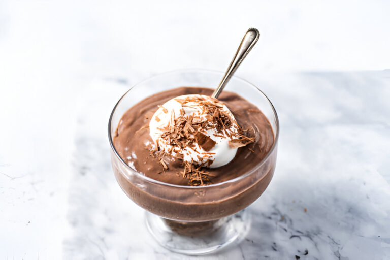 A creamy chocolate mousse topped with whipped cream and chocolate shavings in a glass dish with a spoon