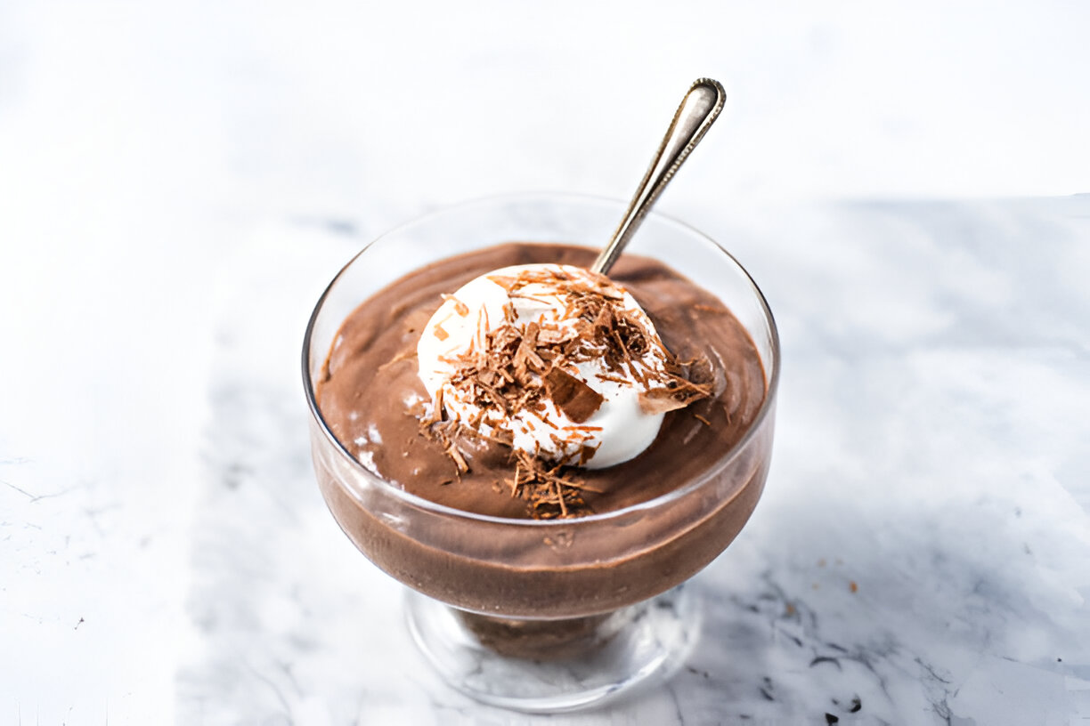 A creamy chocolate mousse topped with whipped cream and chocolate shavings in a glass dish with a spoon