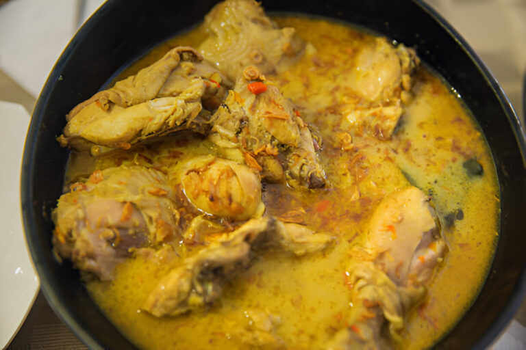 A close-up of a pot filled with chicken pieces in a rich, yellow curry sauce.