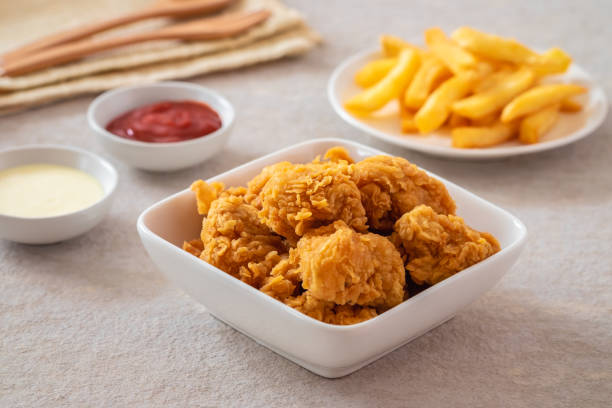 A bowl of crispy fried chicken with dipping sauces and fries in the background.
