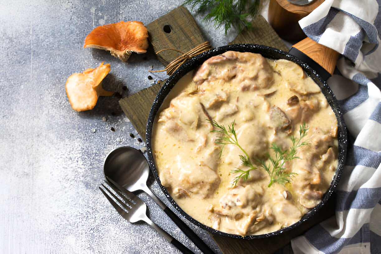 Delicious creamy meat dish served in a black skillet on a wooden board with garnishing.