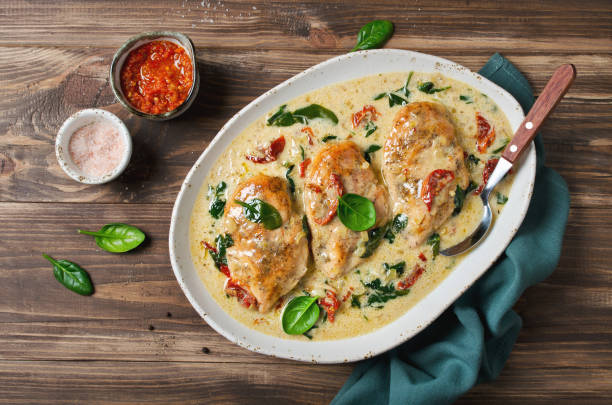 Three chicken breasts in creamy sauce with spinach and sun-dried tomatoes served in a white dish on a wooden table.