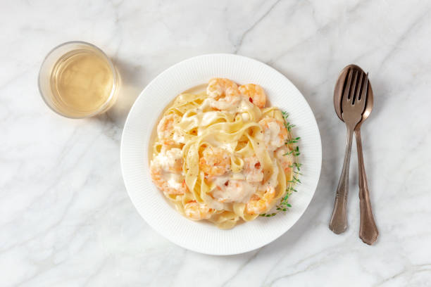 Plate of fettuccine pasta with shrimp in creamy sauce, accompanied by a glass of white wine and cutlery.