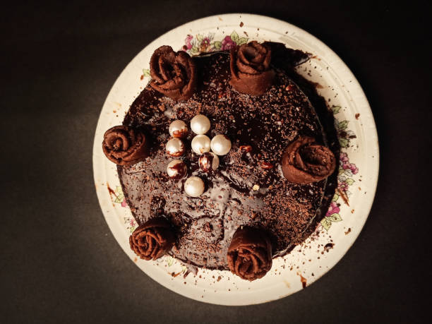 A round chocolate cake decorated with chocolate rosettes and edible pearls on a floral-patterned plate.