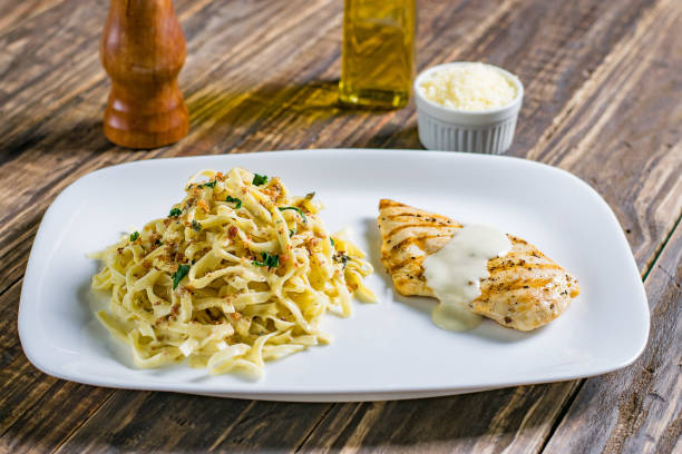 A plate of grilled chicken with a creamy sauce served alongside buttery egg noodles topped with herbs.