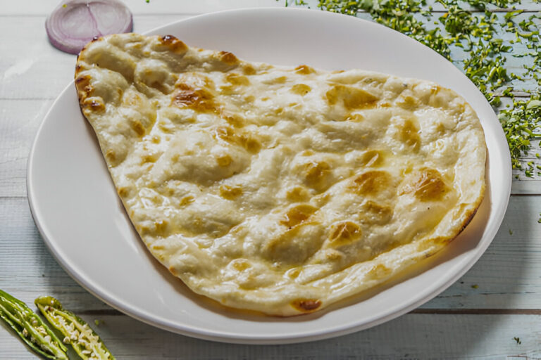 Deliciously cooked naan bread on a white plate with green herbs in the background