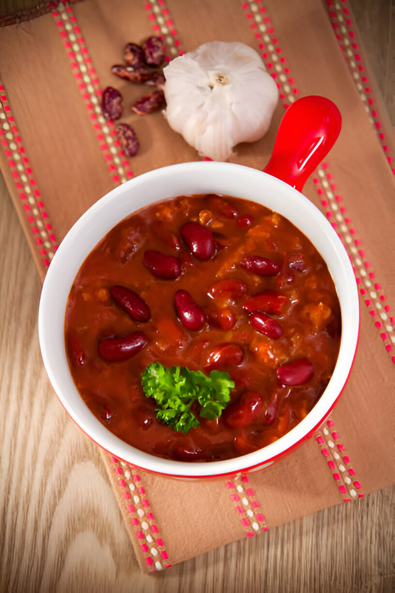 A bowl of chili topped with parsley on a decorative cloth.