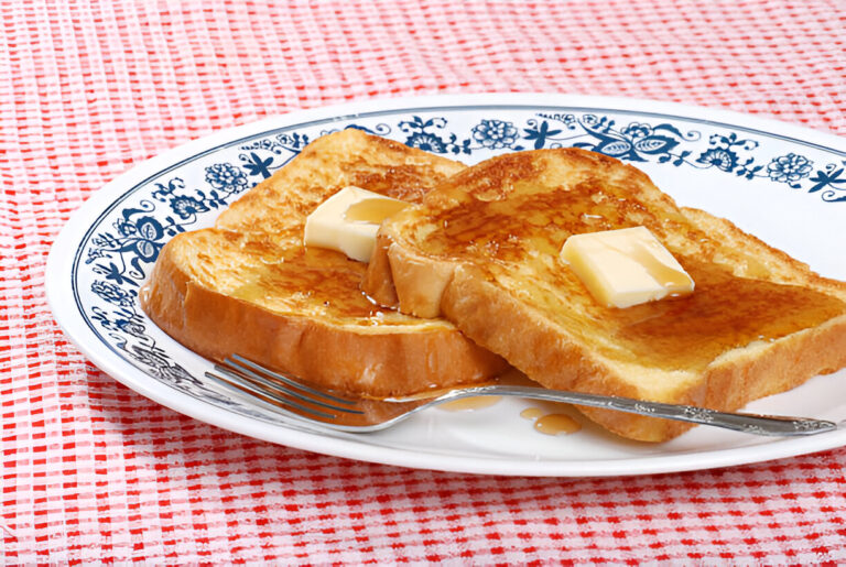 A plate of french toast topped with butter and syrup on a red and white checkered tablecloth.