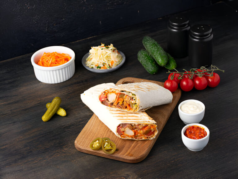 Two flavorful burritos with a variety of vegetables and sauces, served on a wooden cutting board, accompanied by cucumbers, tomatoes, pickles, and side dishes.