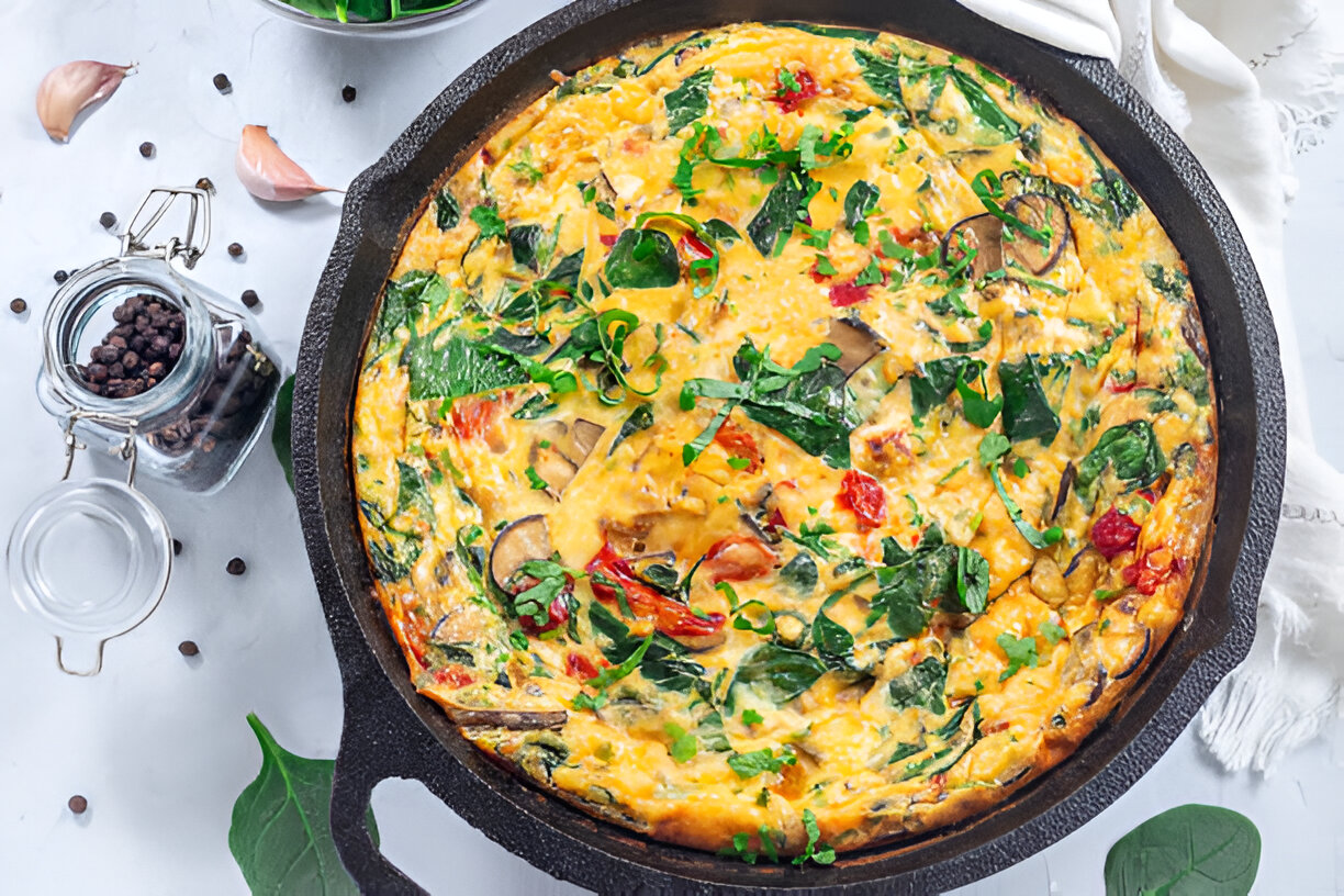 A colorful baked frittata with spinach and tomatoes in a cast iron skillet.