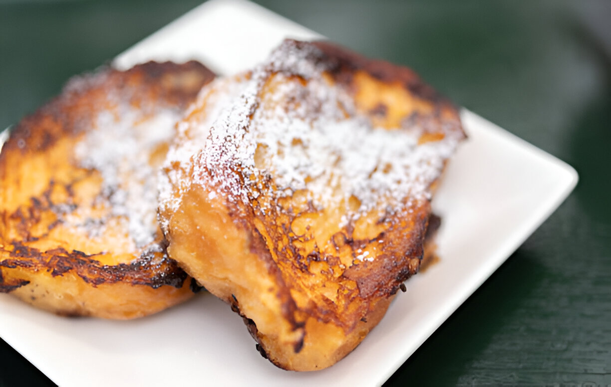 Two pieces of French toast dusted with powdered sugar on a white plate.
