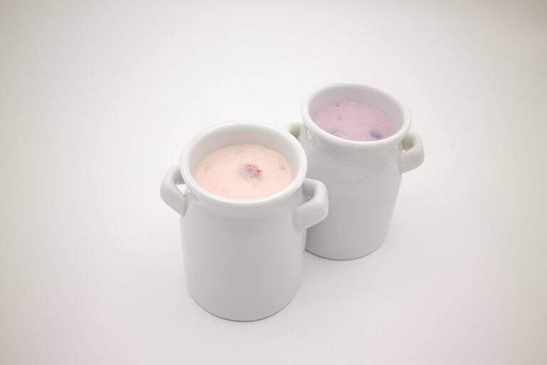 Two small white ceramic containers holding pink and purple yogurt-like desserts.