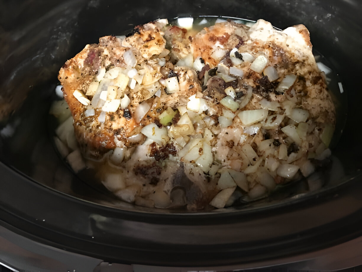Slow cooker with seasoned chicken and chopped onions.