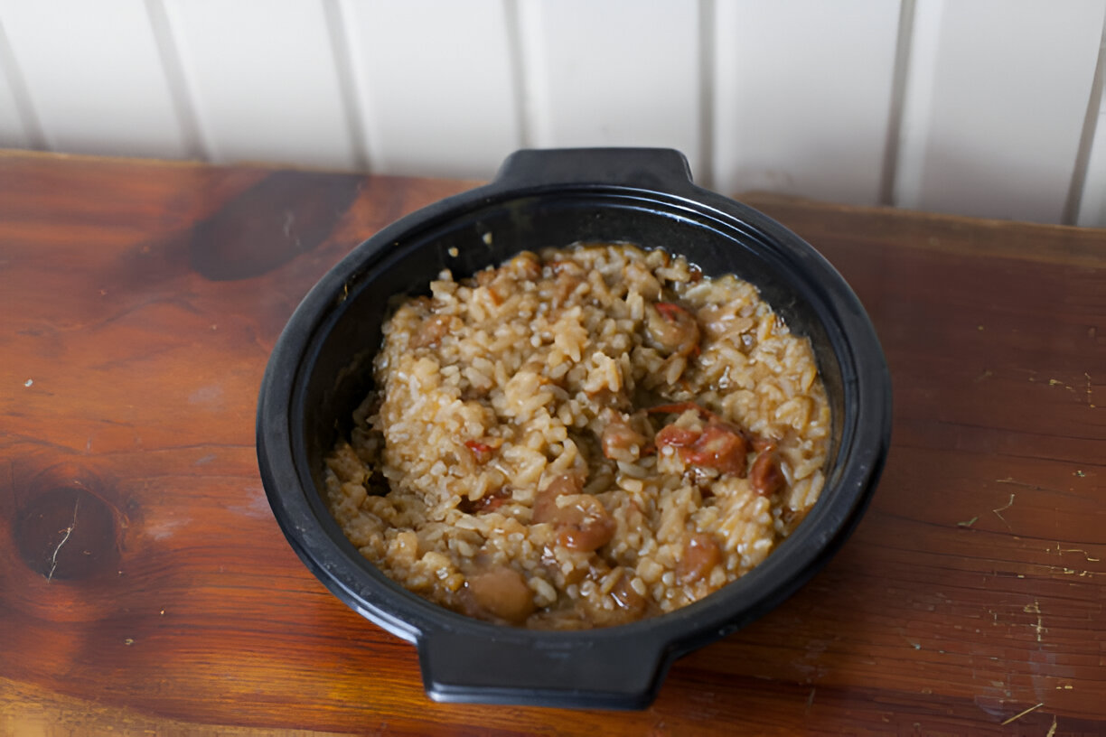 A black bowl filled with rice and pieces of sausage on a wooden table.