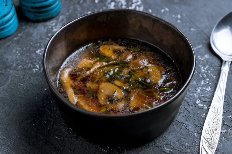 A bowl of soup with herbs and mushrooms on a dark textured surface.