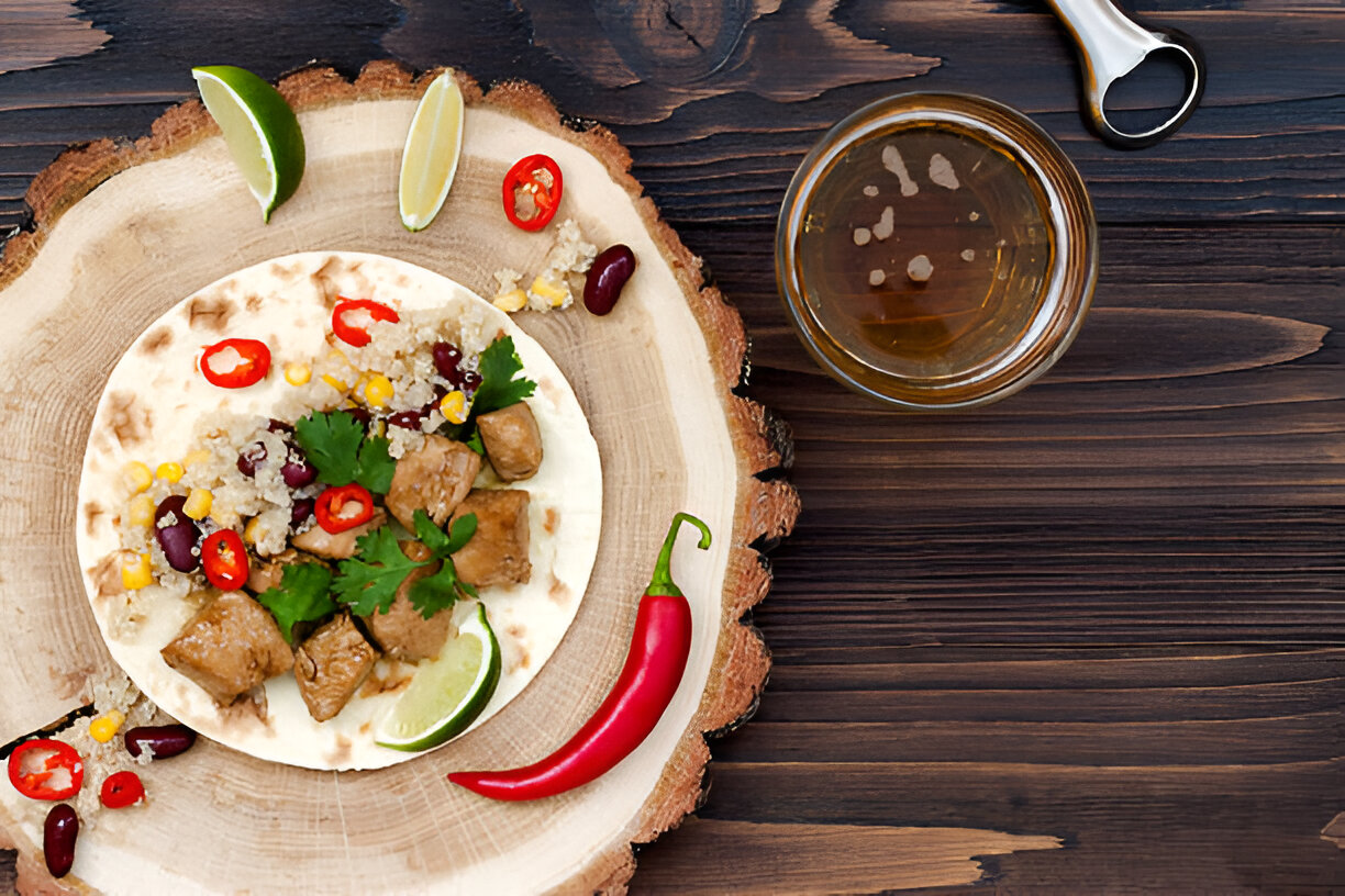A delicious tortilla filled with meat, beans, corn, and garnished with cilantro and chili, placed on a wooden platter next to a glass of beverage.