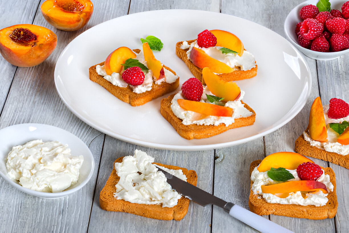 Toast topped with cream cheese, raspberries, and peaches served on a white plate.