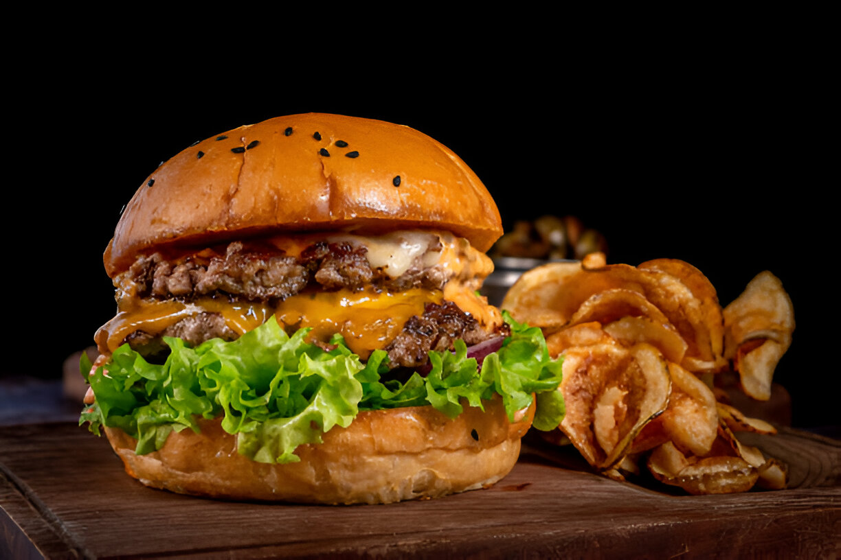 A delicious hamburger with lettuce, onions, and melted cheese, served with crispy potato chips.