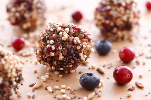 Healthy seed and fruit energy balls surrounded by blueberries and cranberries on a wooden surface.
