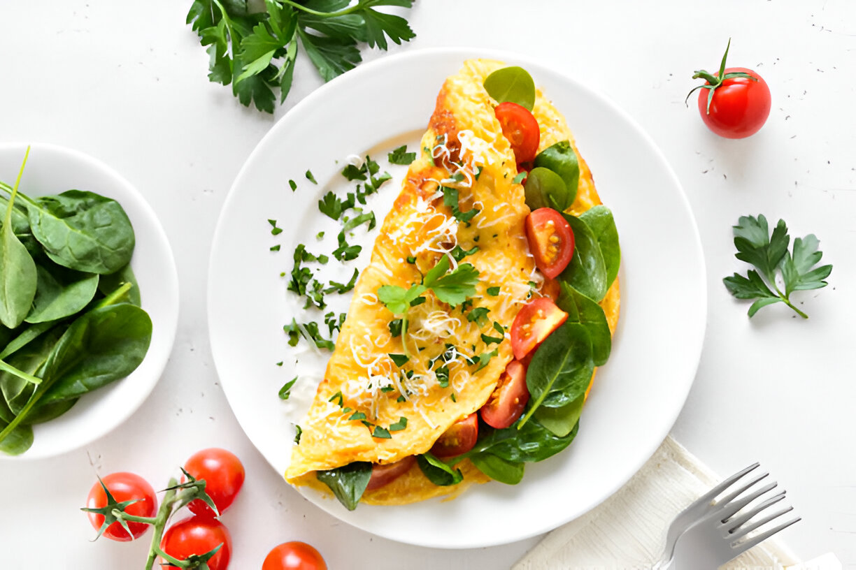A delicious spinach and tomato omelette served on a white plate with fresh parsley and cherry tomatoes.