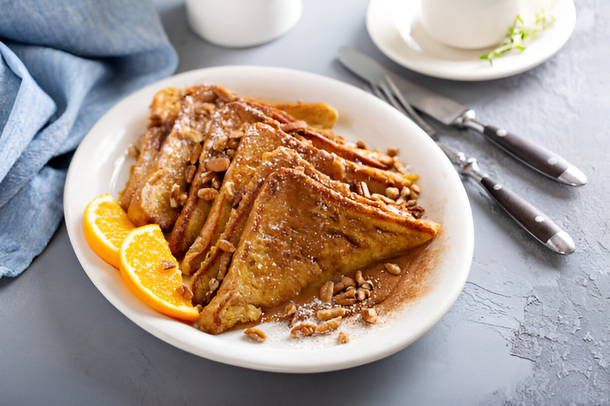 A plate of golden brown French toast garnished with nuts and orange slices.