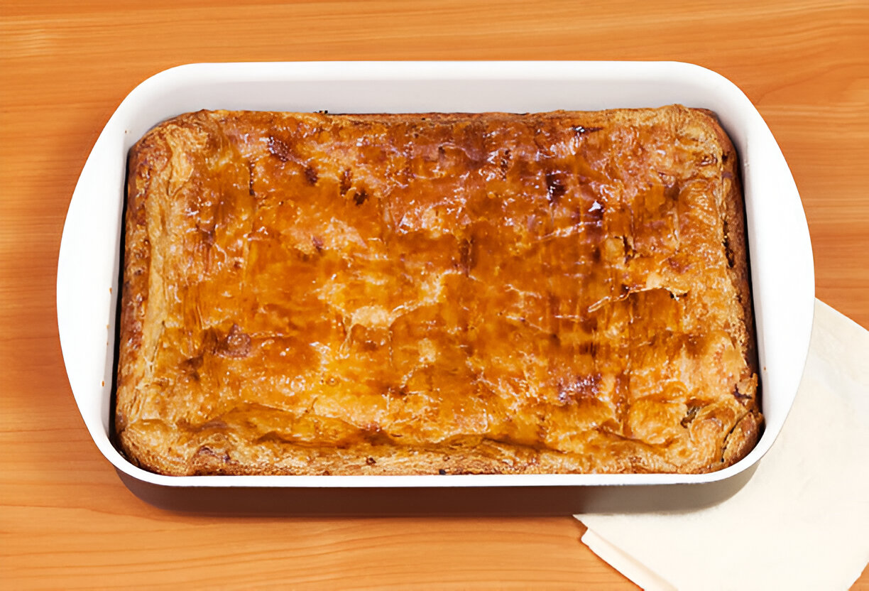 A freshly baked pastry in a white dish resting on a wooden table.
