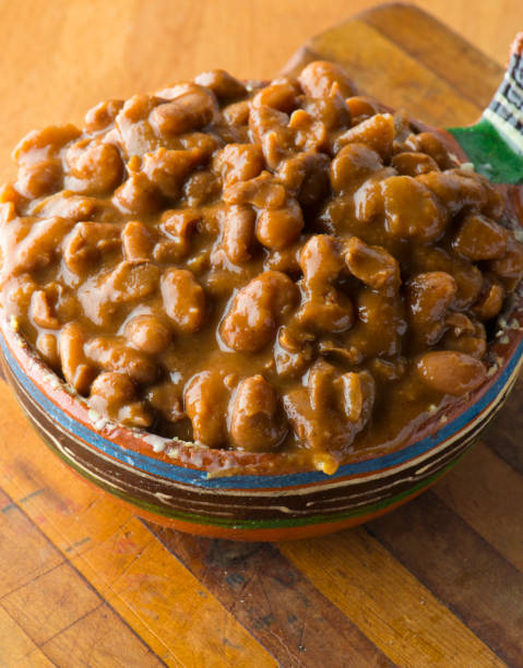 A bowl of brown beans in a decorative ceramic dish on a wooden cutting board.