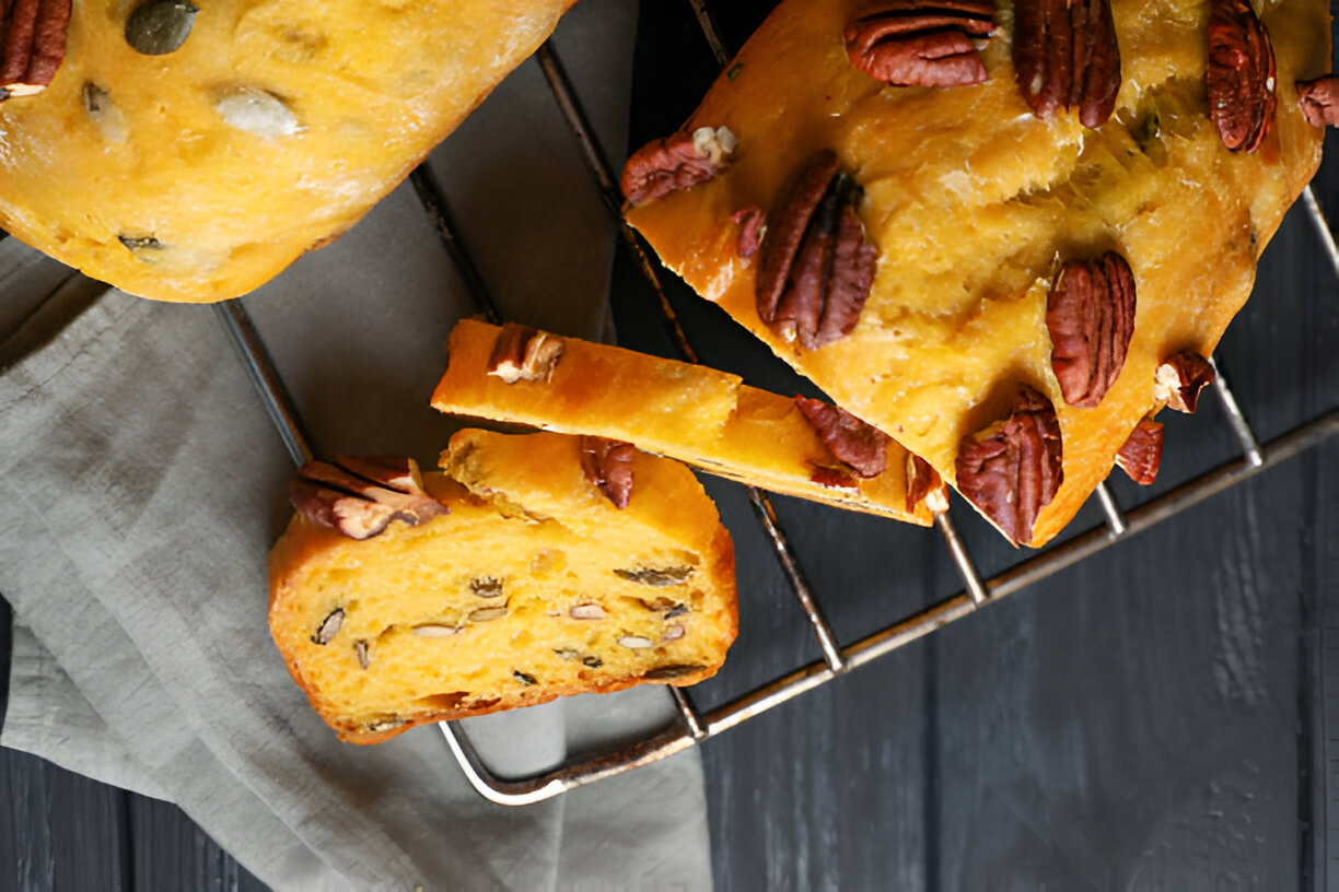 Freshly baked loaf of bread topped with pecans on a cooling rack
