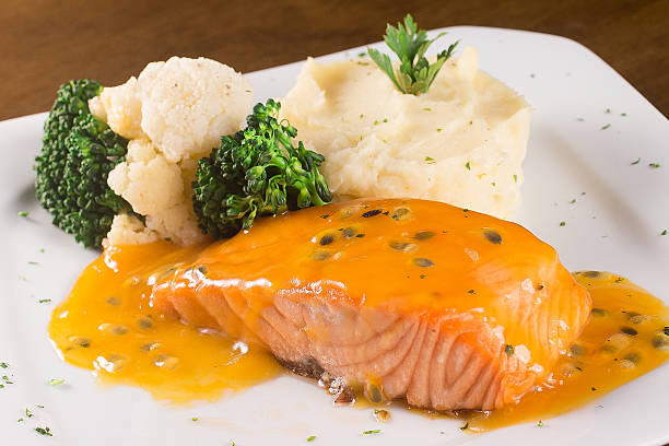 A plate of salmon with a passion fruit sauce accompanied by steamed broccoli, cauliflower, and mashed potatoes.