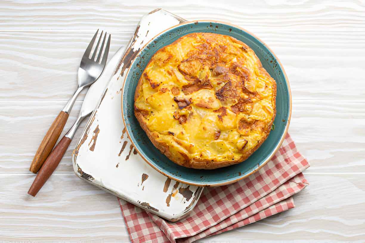 A delicious Spanish tortilla served on a turquoise plate, accompanied by silver forks, on a rustic white wooden surface.