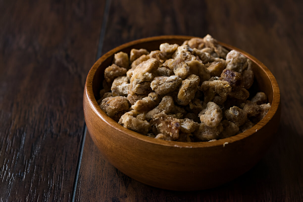 A wooden bowl filled with crunchy snacks placed on a wooden surface.