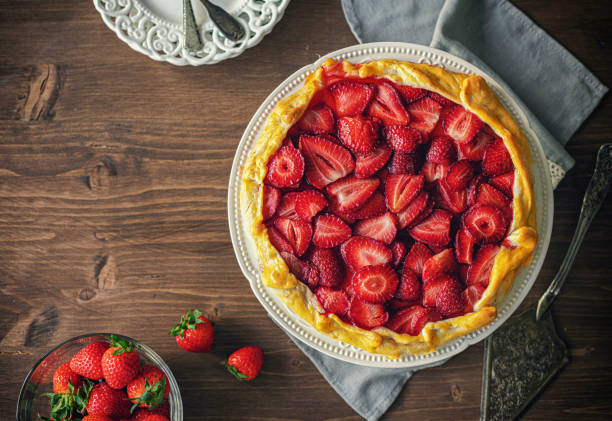 A freshly baked strawberry tart on a rustic wooden table, surrounded by fresh strawberries.