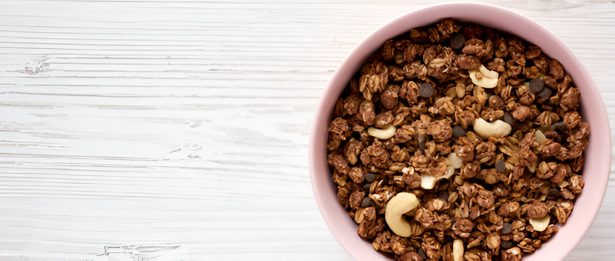 A bowl of granola with nuts and chocolate chips on a wooden surface.
