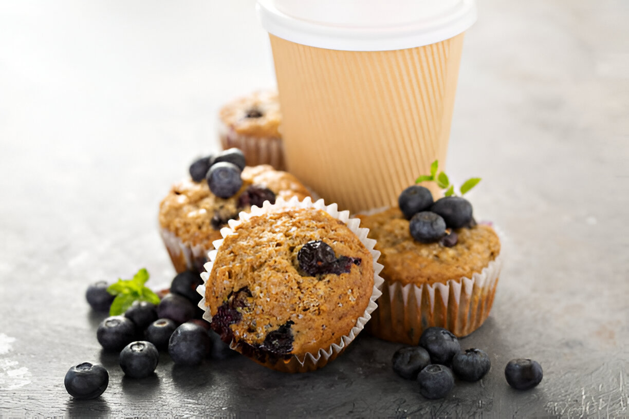 Fresh blueberry muffins with a coffee cup on a textured surface.