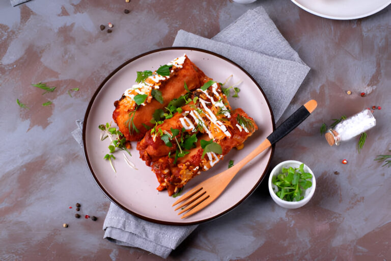 A plate of delicious enchiladas topped with cilantro and a drizzle of sauce, alongside a small bowl of chopped green onions.