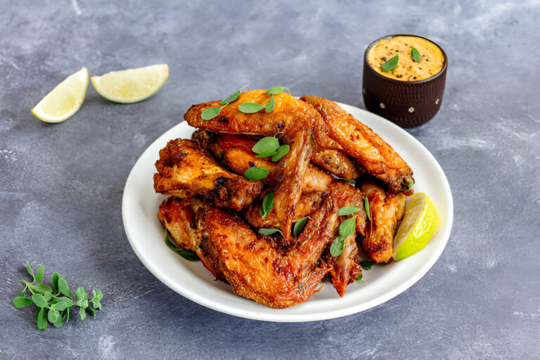 A plate of crispy grilled chicken wings garnished with herbs, accompanied by a lime wedge and a small cup of sauce.