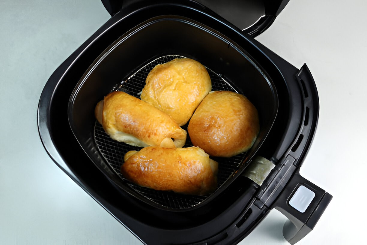 Four freshly cooked bread rolls in an air fryer basket.