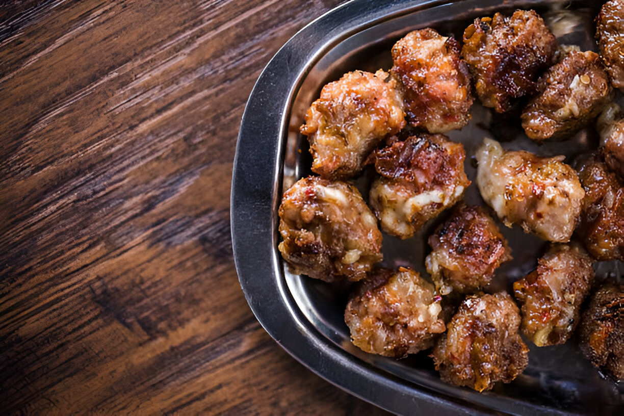 A plate of golden-brown meatballs served in a stainless steel dish on a wooden table.