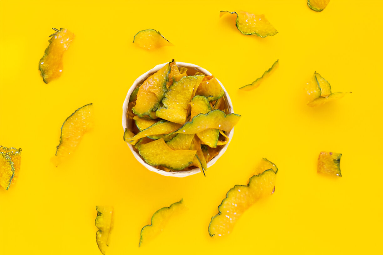 A bowl of crispy, vibrant yellow melon peels surrounded by scattered peels on a bright yellow background.