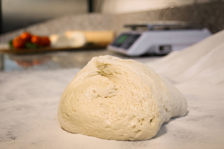 A ball of dough resting on a marble countertop with flour scattered around it.