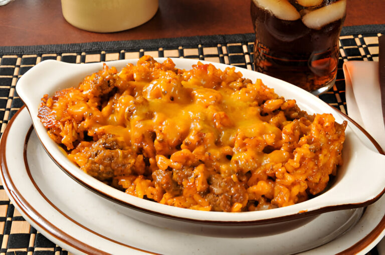 A delicious dish of cheesy rice and beef served in a white ceramic bowl, placed on a dark placemat next to a glass of iced cola.