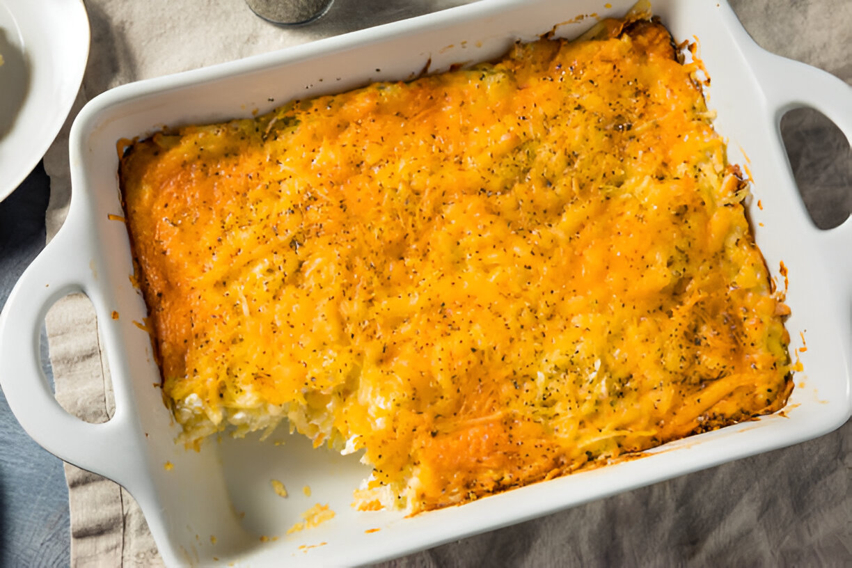 A cheesy baked casserole with golden brown topping in a white dish, partially served.