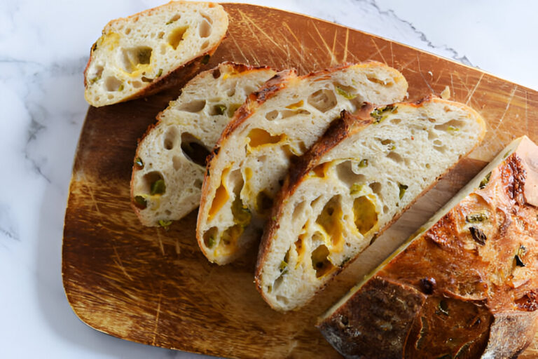 Sliced artisan bread with green peppers and cheese on a wooden cutting board